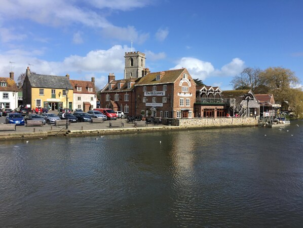 A riverside town with historic buildings, a prominent tower, and a pub named 'The Old Crane'.