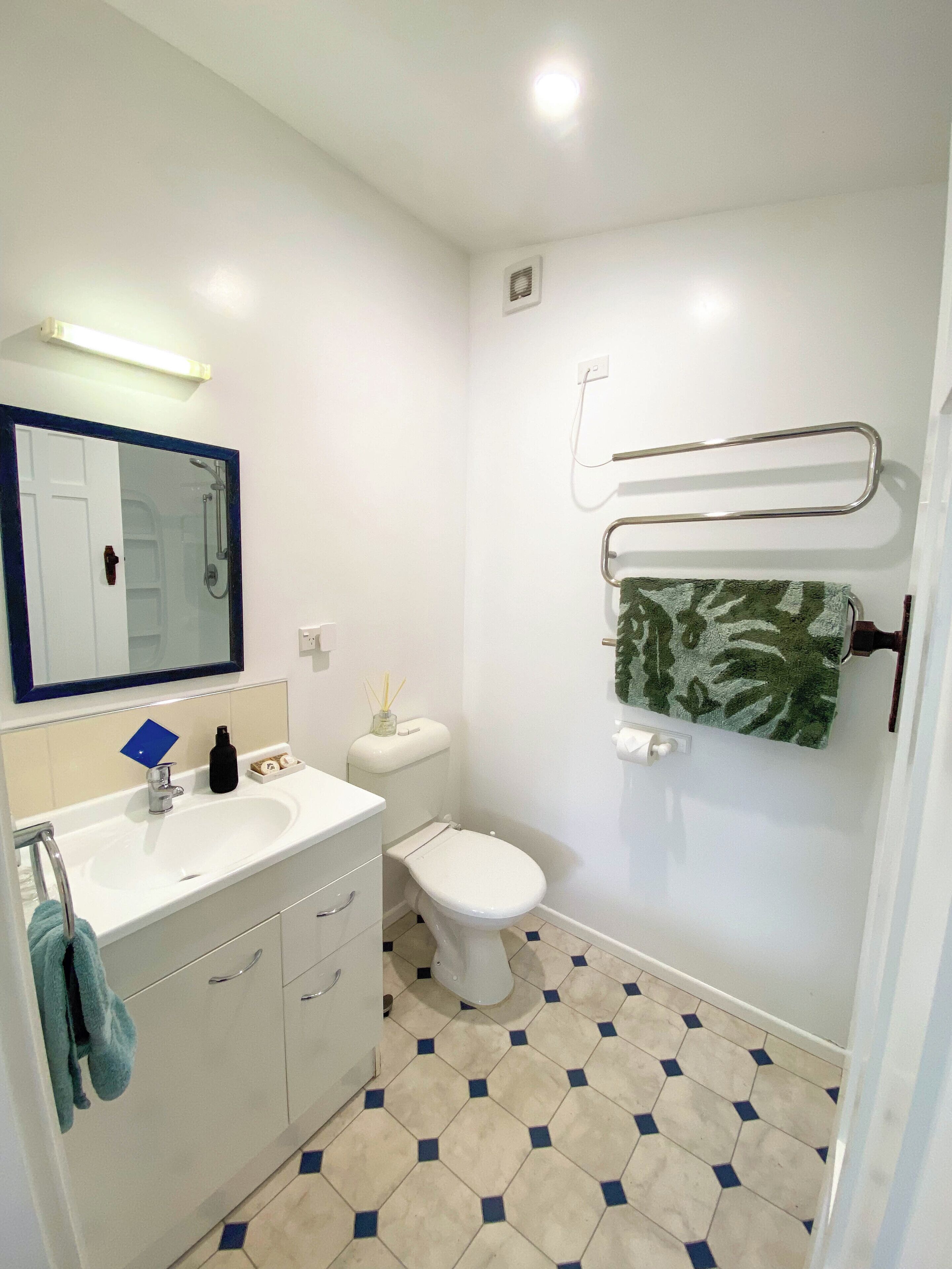 Un baño con lavamanos blanco, espejo, inodoro y toallero.