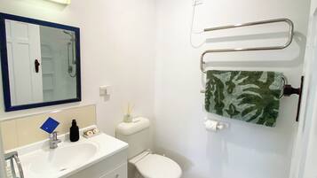 Un baño con lavamanos blanco, espejo, inodoro y toallero.