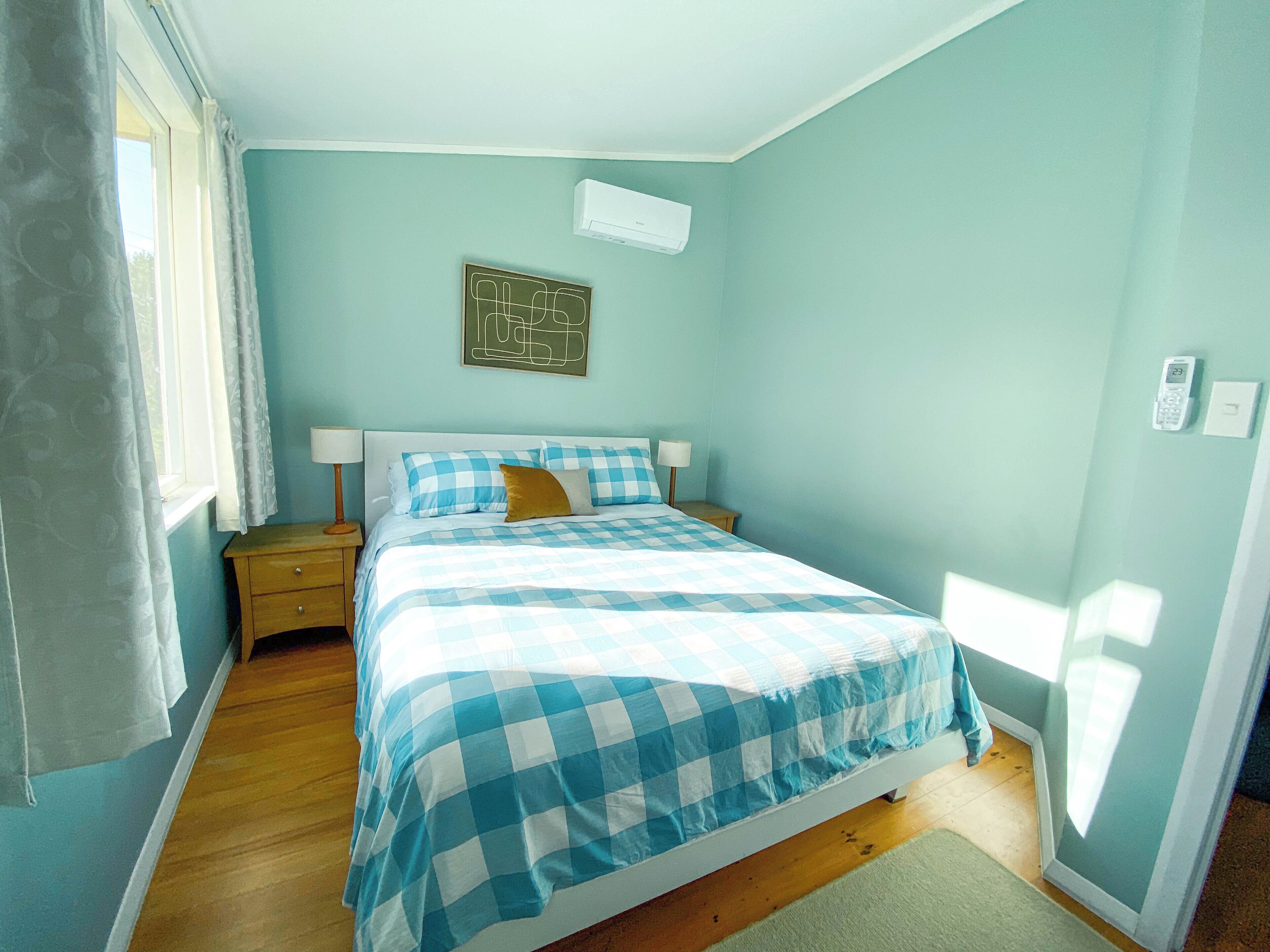 Une chambre à coucher comprenant un lit, une table de chevet, un climatiseur fixé au mur et un tableau encadré.
