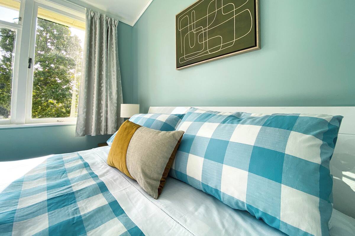 A bedroom with a bed, a window with curtains, and a wall-mounted artwork.