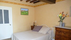 Een slaapkamer met een bed, een kaptafel, een vaas met bloemen en een schilderij aan de muur.