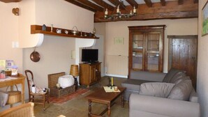 Een gezellige woonkamer met een houten plafond, een televisie, een bank en een eethoek met rieten meubels.