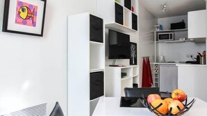 A modern kitchen with white cabinets, a dining table with a black chair, and a fruit bowl. - Air-conditioned studio with a garage near the Port of Nice (Nice)