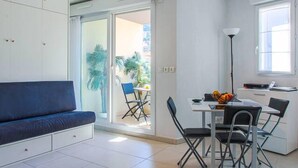 A modern living room with a sofa, a dining area with a table and chairs, and a sliding glass door leading to a balcony with plants. - Air-conditioned studio with a garage near the Port of Nice (Nice)