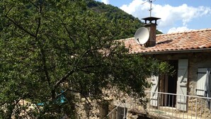 A rustic stone building with a tiled roof, a satellite dish, and a small outdoor seating area with white plastic chairs and a table. - Renovated stone house private next to river, Welcoming and very well equipped (Juvinas)