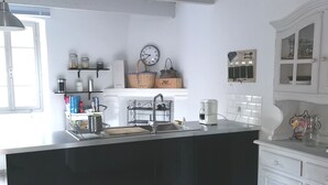 A modern kitchen with a black island, white cabinetry, and a wooden floor. - Renovated stone house private next to river, Welcoming and very well equipped (Juvinas)