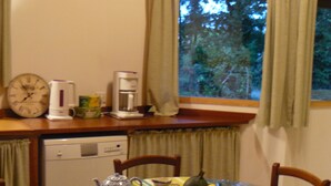 A compact kitchen with a dining table, chairs, a clock, a coffee maker, and a dishwasher. - LA LANDAISE DU CHARPENTIER <br>17 Chemin Traouquevert <br>40430 CALLEN  (Callen)