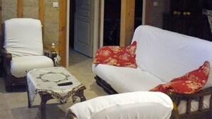 A cozy room with a wooden ceiling, a white sofa with red cushions, a white armchair, and a small table with a patterned tablecloth. - LA LANDAISE DU CHARPENTIER <br>17 Chemin Traouquevert <br>40430 CALLEN  (Callen)