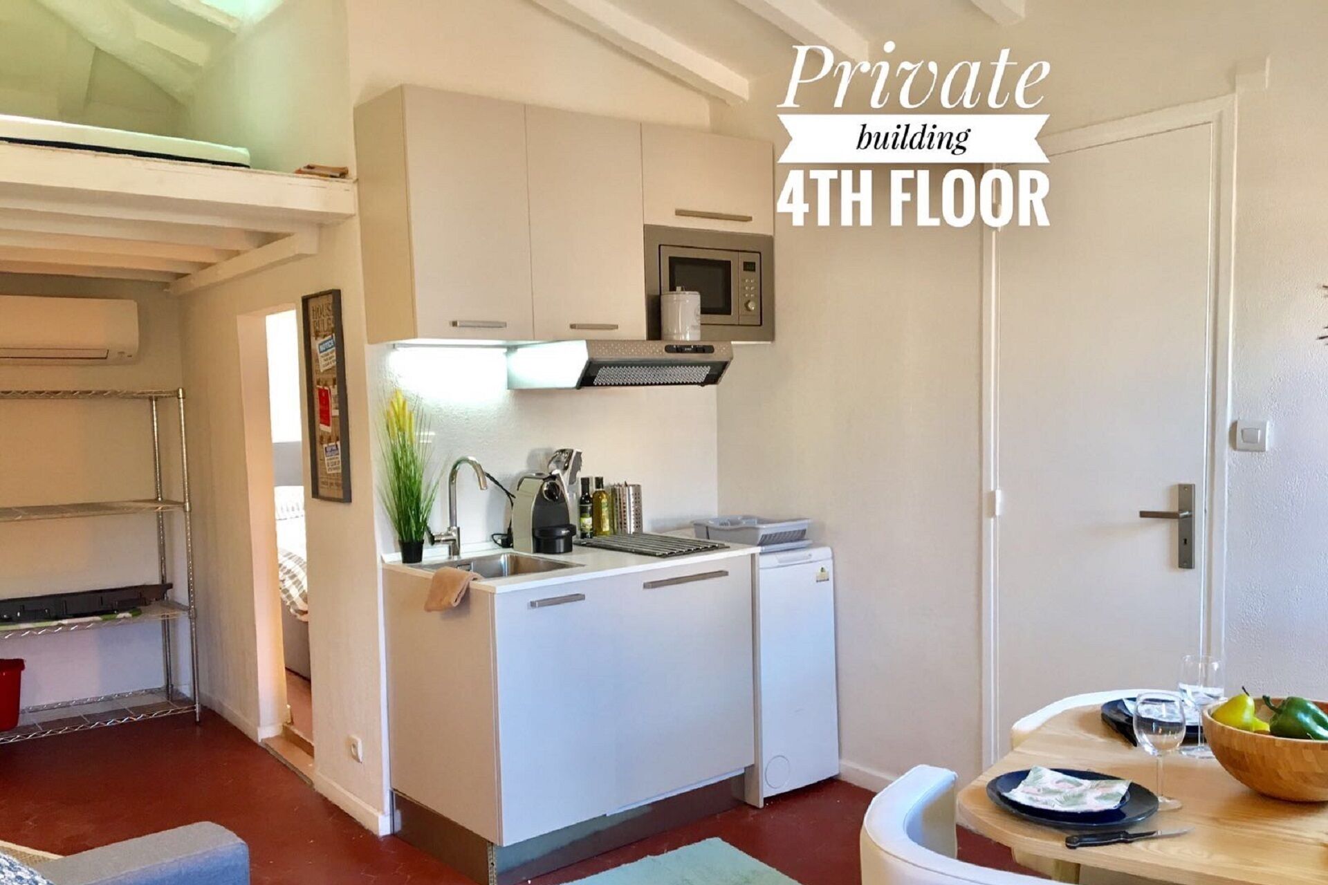 Een compacte keuken met witte kasten, een magnetron en een spoelbak. Er is een klein eethoekje met een tafel en stoelen. De tekst 'Private building 4th floor' is zichtbaar.
