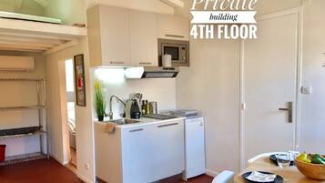 Een compacte keuken met witte kasten, een magnetron en een spoelbak. Er is een klein eethoekje met een tafel en stoelen. De tekst 'Private building 4th floor' is zichtbaar.