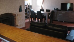 A living room with a fireplace, a dining area with a table and chairs, a television, and a bookshelf.