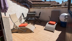 Een terras op het dak met een tafel, stoelen, een ligbed en een boiler.