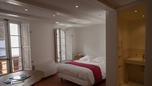 Een slaapkamer met een bed, nachtkastje, raam en een badkamer met wastafel.