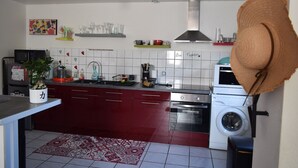 Une cuisine compacte équipée d’un four à micro-ondes, d’une cuisinière et d’un lave-linge. On y trouve une plante en pot et un chapeau décoratif posés sur le plan de travail.