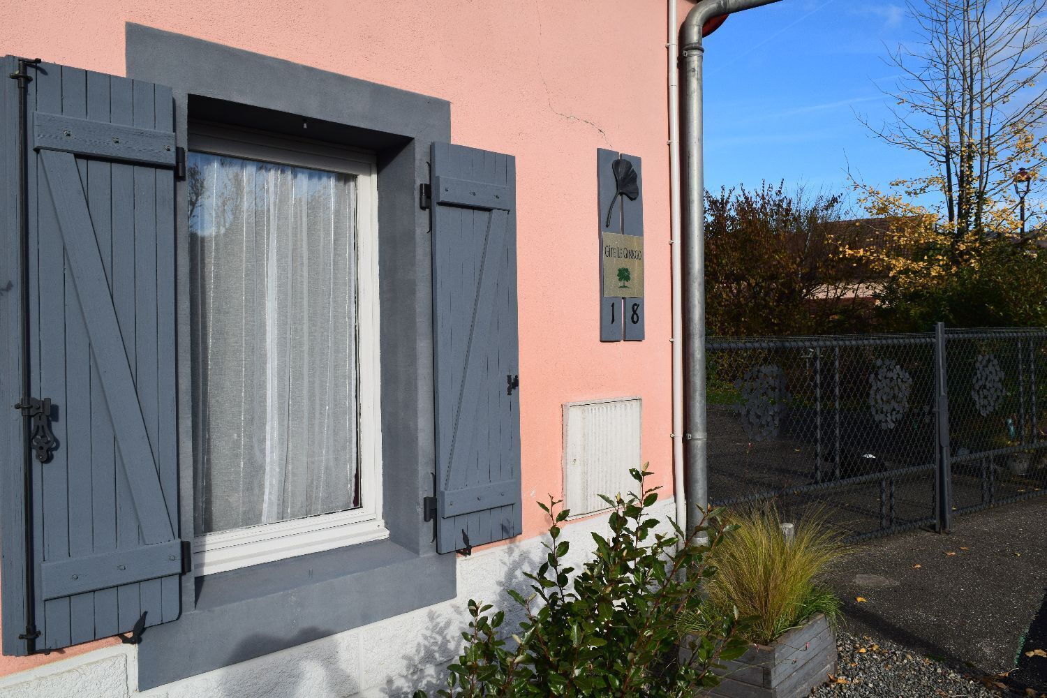 Un bâtiment à la façade rose, aux volets gris et à l’enseigne indiquant « Café Le Chêne 18 ».