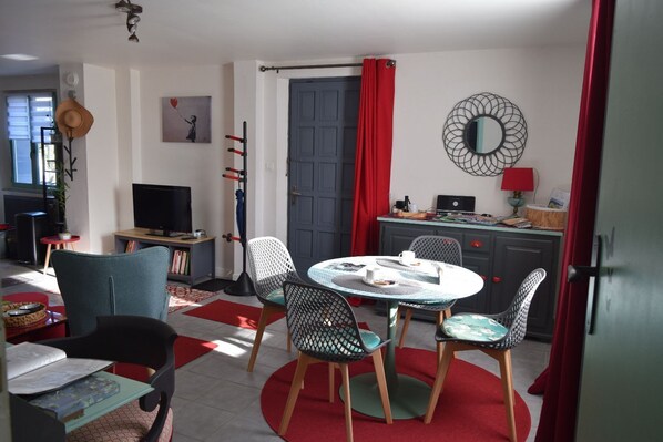 A cozy living room with a round table, chairs, a television, and a bookshelf.