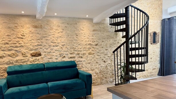 Una sala de estar moderna con una pared de piedra, un sofá color turquesa, una mesa de centro redonda y una escalera en espiral.