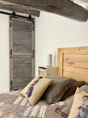 Une chambre à coucher avec une tête de lit en bois, un lit avec une literie à motifs, une table de chevet avec une lampe et une armoire en bois dotée d’une porte coulissante.