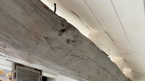 Un dormitorio con techo inclinado, una cama con cabecera de madera, una mesita de noche con lámpara y una puerta que da a otra habitación.