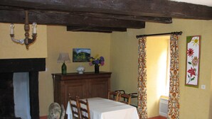 A dining area with a table set for four, wooden chairs, a cabinet with a vase of flowers, and a painting on the wall. - Cottage in the heart of the Périgord-Limousin Regional Nature Park (Dournazac)