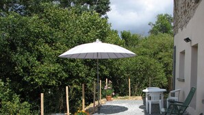 A patio area with a barbecue grill, a table, two chairs, and an umbrella. - Cottage in the heart of the Périgord-Limousin Regional Nature Park (Dournazac)