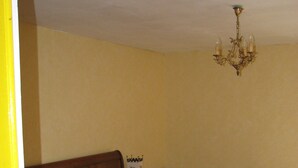 A bedroom with a wooden bed, a green patterned rug, a yellow wall, and a chandelier. - Cottage in the heart of the Périgord-Limousin Regional Nature Park (Dournazac)