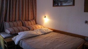 Un dormitorio con cama, almohadas, una mesita de noche, una lámpara de pared y un cuadro en la pared.
