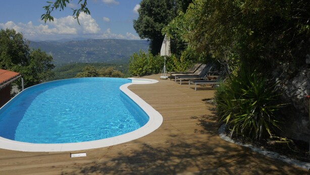 A swimming pool with a wooden deck, lounge chairs, and a view of mountains.