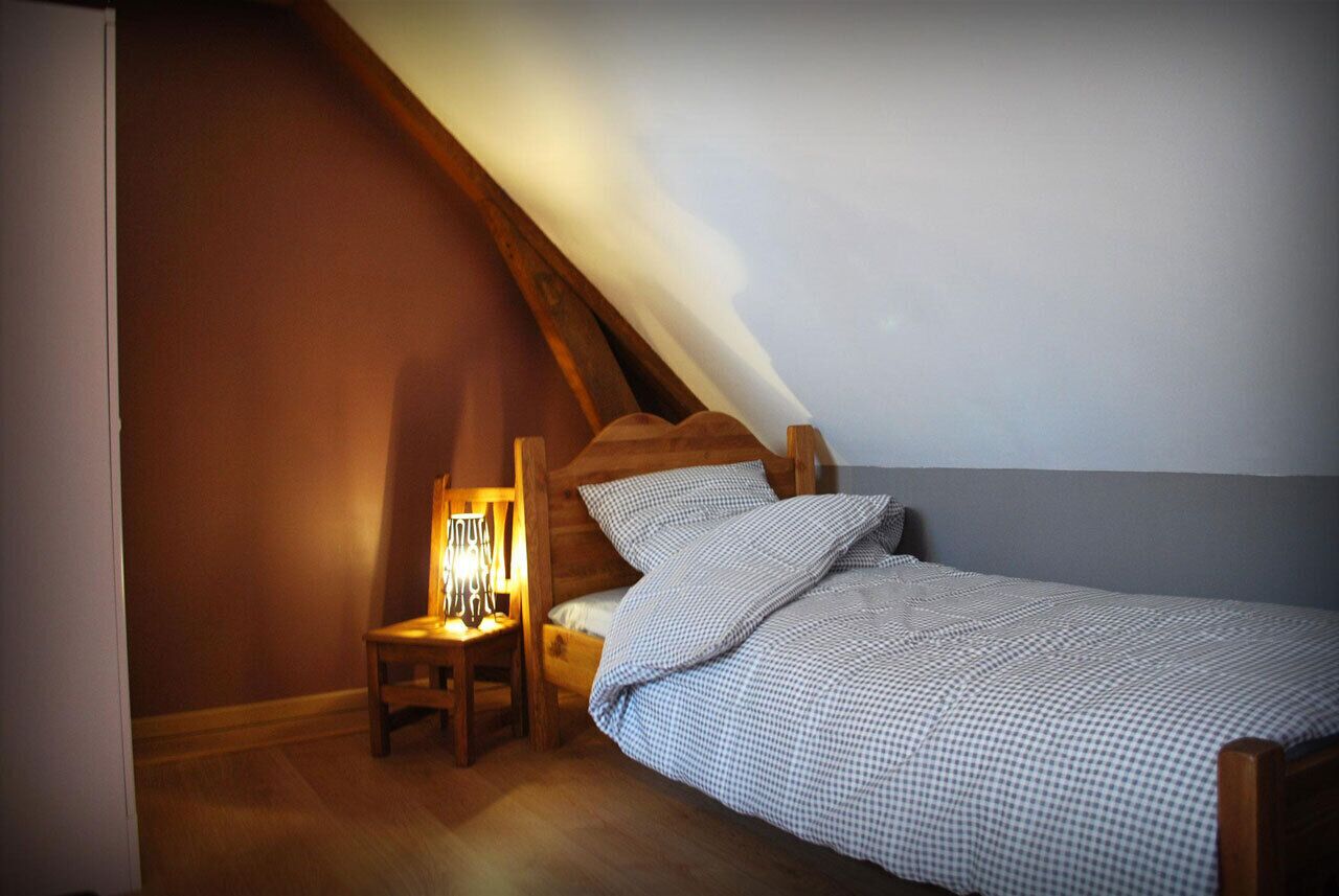 A small, cozy bedroom with a sloped ceiling, a wooden bed, a nightstand with a lamp, and a chair.