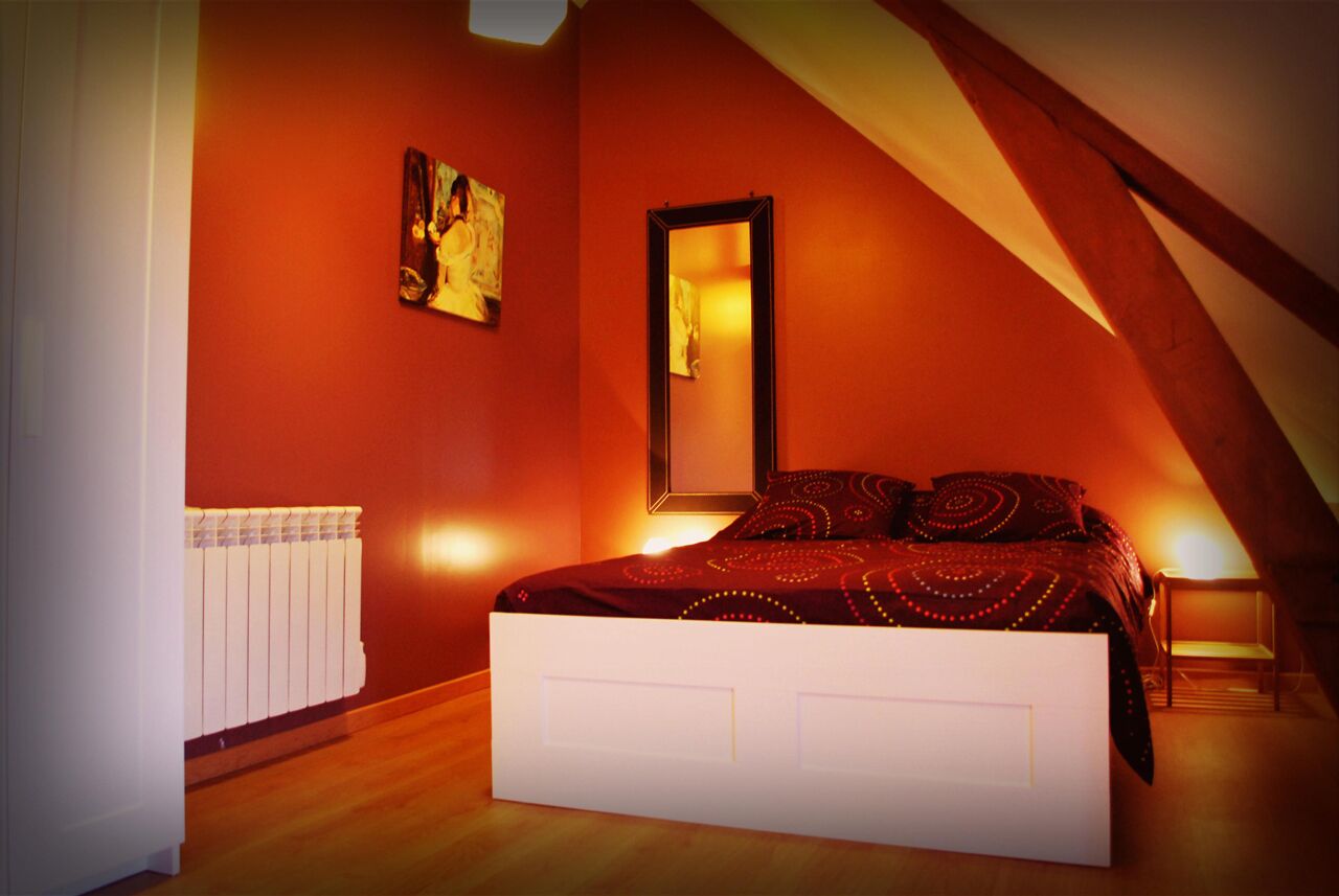 Un dormitorio con techo inclinado, una cama con ropa de cama estampada, un radiador y un cuadro en la pared.