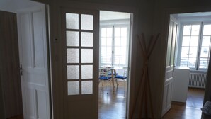 Una stanza con pavimento in legno, una porta bianca con vetri decorati e un angolo ristoro con tavolo e sedie, più un termosifone.