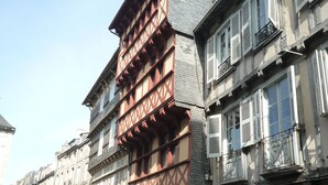 Una strada acciottolata fiancheggiata da edifici storici caratterizzati da un'architettura europea tradizionale, con travi a vista e persiane.