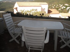 A white outdoor patio with a table and four chairs, overlooking a hillside with buildings. - Vacation rental in LA CROIX VALMER: private domain with swimming pool (La Croix-Valmer)