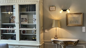 Una habitación con una gran estantería llena de libros, una lámpara de mesa y un cuadro en la pared.