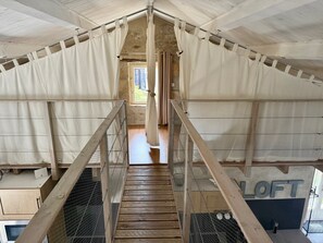 Habitación estilo loft con escalera de madera, cortinas blancas y una mosquitera.