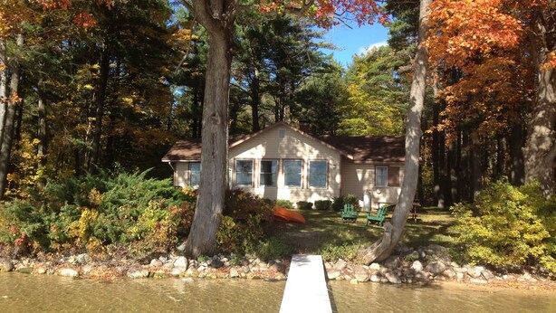 Une cabane avec un quai s’avançant dans un lac aux eaux limpides, entourée d’un paysage automnal aux couleurs flamboyantes.