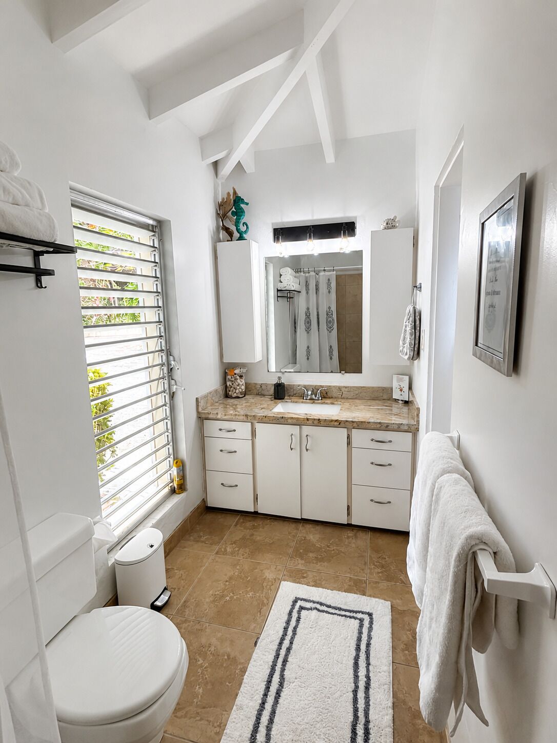 A bathroom with a toilet, sink, vanity, and a window with blinds.