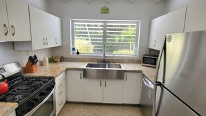 Une cuisine moderne avec des meubles blancs, un réfrigérateur en acier inoxydable, une cuisinière à gaz et une fenêtre équipée de stores.