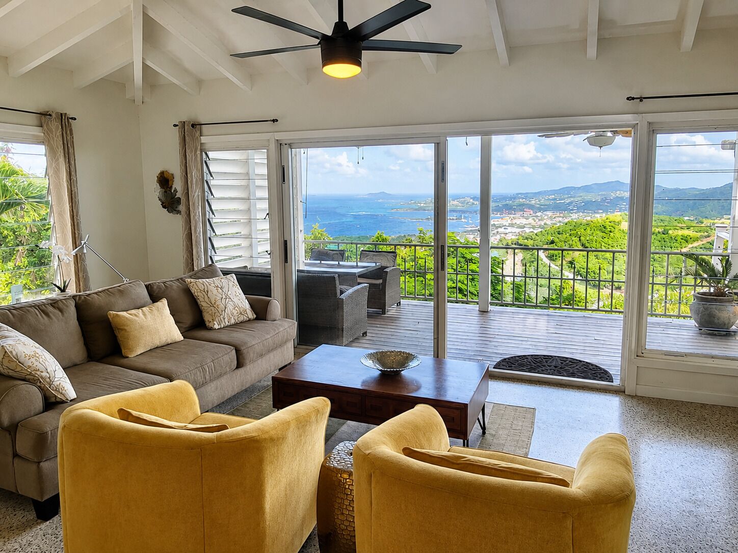 A living room with a sofa, two armchairs, a coffee table, and a balcony with a view of the landscape.