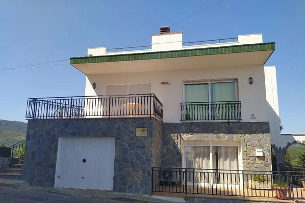 Une maison à deux étages avec une façade en pierre, un niveau supérieur blanc et un balcon doté de balustrades noires.