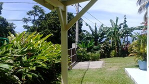 A garden with various tropical plants, a concrete pathway, and a white structure. - F2 air-conditioned with ocean view (Trois Rivieres)