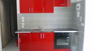 A kitchen with red cabinets, a stainless steel sink, and a black oven. - F2 air-conditioned with ocean view (Trois Rivieres)