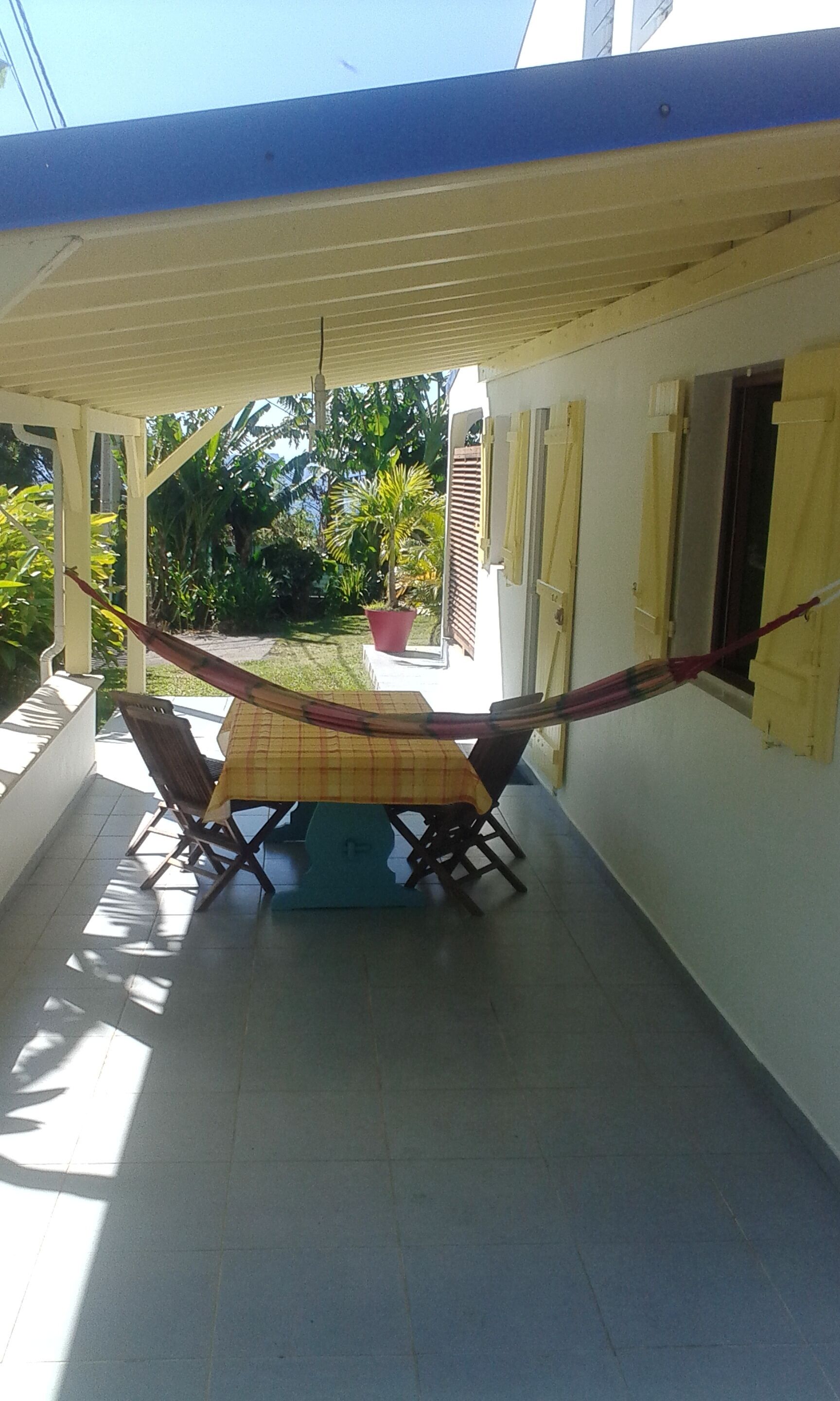 A covered patio with a table and chairs, a hammock, and a view of a garden and house.