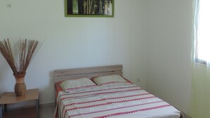 A bedroom with a bed, a nightstand, a vase with dried plants, and a framed picture on the wall. - F2 air-conditioned with ocean view (Trois Rivieres)