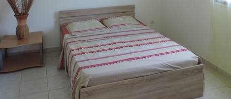 A bedroom with a bed, a nightstand, a vase with dried plants, and a framed picture on the wall.