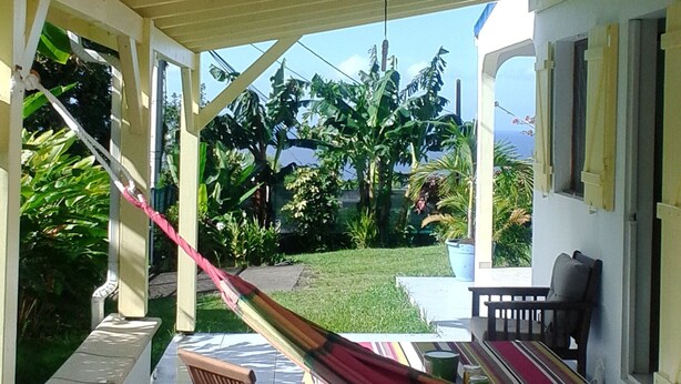 A covered outdoor area with a hammock, chairs, and a table. - F2 air-conditioned with ocean view (Trois Rivieres)