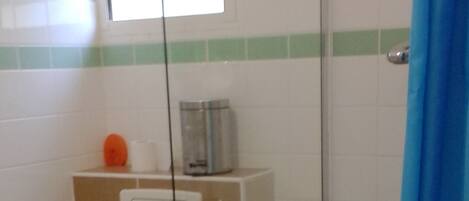 A bathroom with a toilet, a glass shower enclosure, and a window with blinds.
