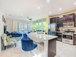 A modern kitchen with stainless steel appliances, a central island, and a dining area with blue chairs.