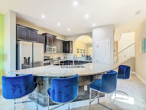 A modern kitchen with dark cabinets, stainless steel appliances, a granite countertop, and blue chairs.